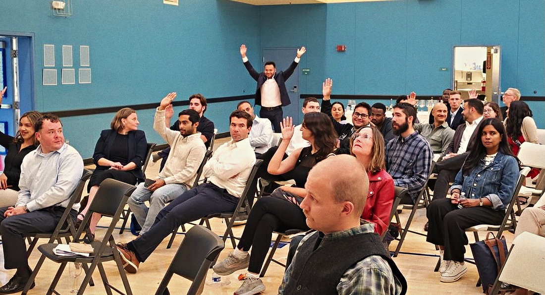 The hall during a talk seen from the side: rows of seated people, several with a hand raised.